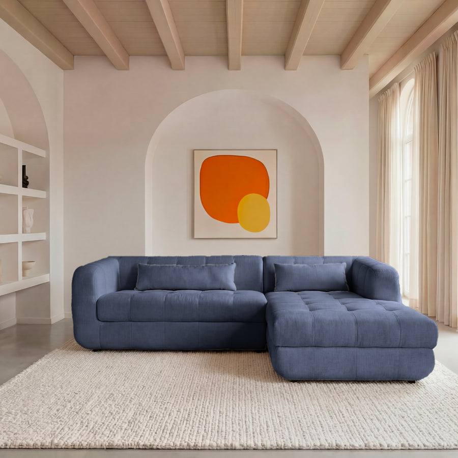 Canapé Arlette d'angle en tissu bleu marine, salon avec bibliothèque murale blanche.