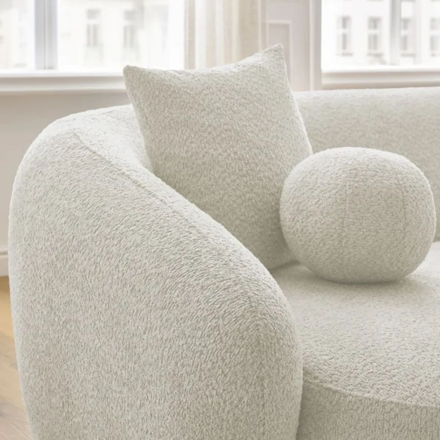 Gros plan sur l'accoudoir arrondi et coussin du canapé Ashley en bouclette blanche.
