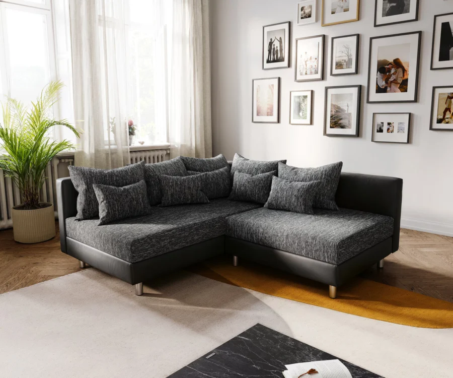 Canapé Clovis d'angle en tissu anthracite chiné et simili cuir noir, devant une galerie de cadres photo.