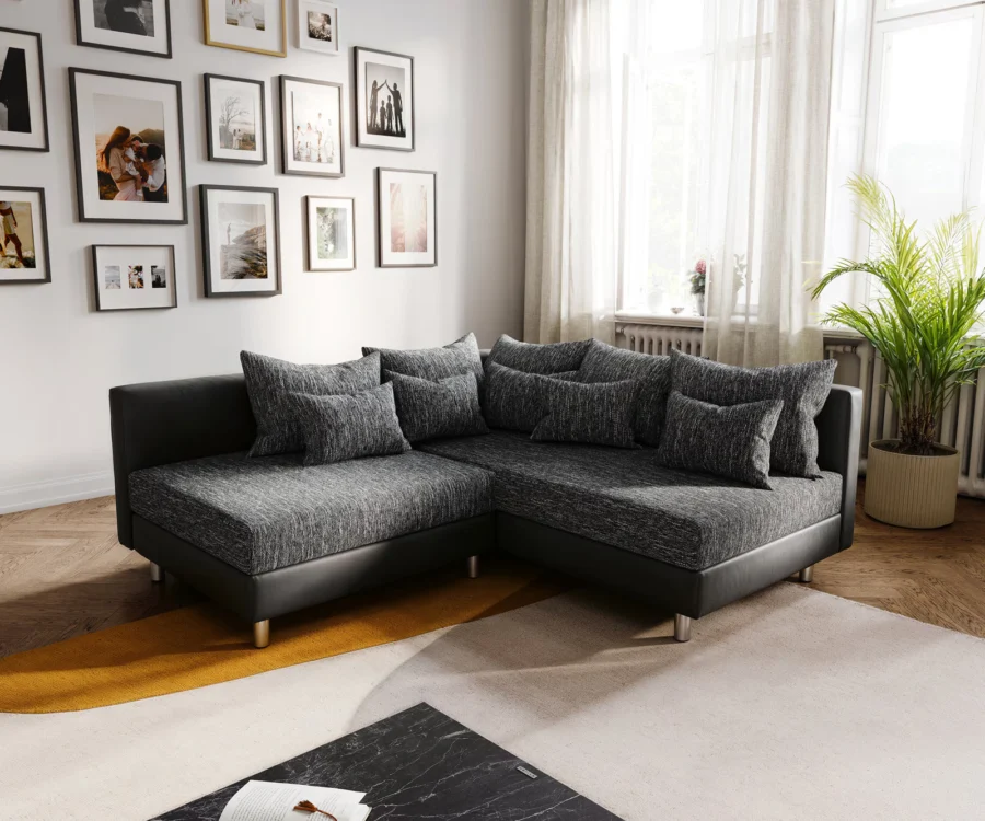 Canapé Clovis d'angle en tissu anthracite chiné et simili cuir noir, placé contre un mur de cadres.