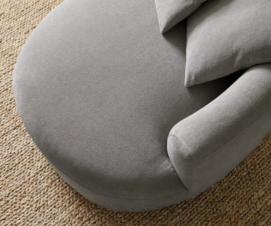 Gros plan de l'assise grise bouclette, de l'accoudoir arrondi et d'un coussin.