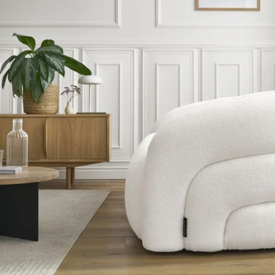Fauteuil Elina blanc arrondi dans un salon moderne, meuble en bois, plante.