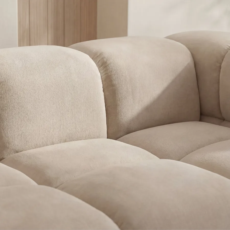 Gros plan du velours texturé beige clair et des accoudoirs arrondis du canapé