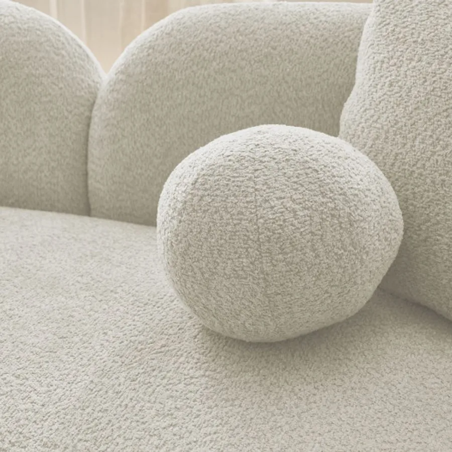 Gros plan sur les coussins ronds et l'assise du canapé Hailey blanc cassé bouclette.