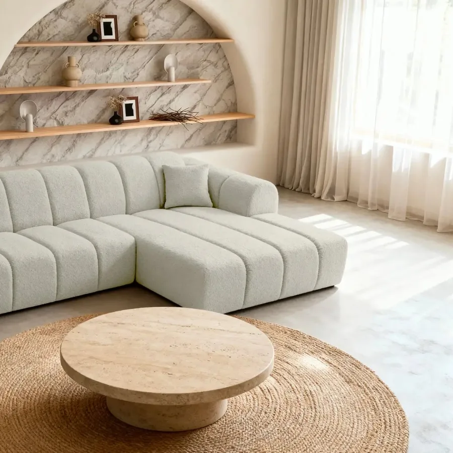 Canapé Laura d'angle en tissu beige clair, dans un salon avec étagères arrondies en marbre.