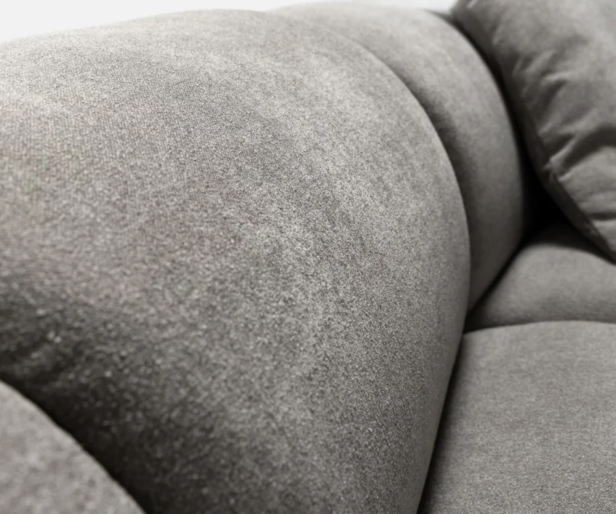Gros plan d'un accoudoir gris arrondi et d'un coussin en tissu doux.