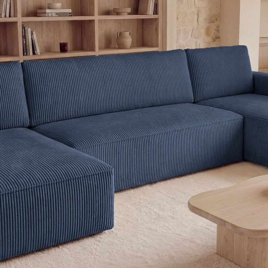 Canapé Maurie bleu en tissu côtelé vu de trois quarts, avec accoudoirs larges et profondeur visible