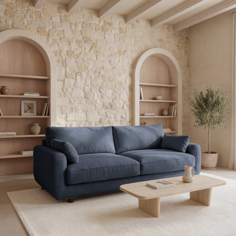 Canapé Stella bleu foncé dans un salon avec étagères arrondies et murs en pierre.